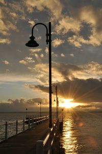 Silhouette street light by sea against sky during sunset