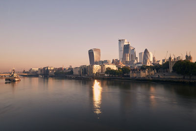 Scenic view of river by buildings against sky during sunset