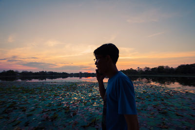 Side view of man standing on shore against sky during sunset