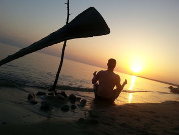 Silhouette man sitting on beach against sky during sunset