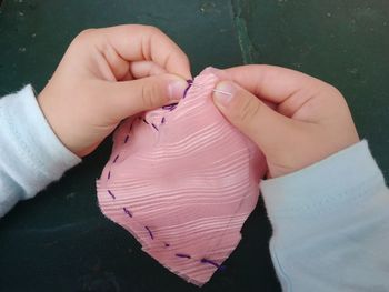 Cropped hands of child stitching fabric on table