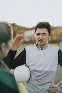 Female instructor explaining to male athlete while standing in sports field