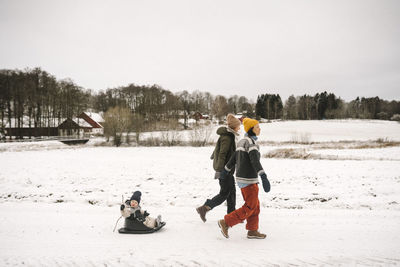 Full length of lesbian mothers pulling daughter while walking on snow