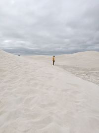 Distant view of man standing on sand dune against cloudy sky