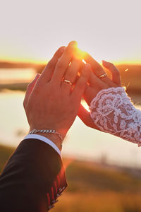 Midsection of couple holding hands against sky during sunset