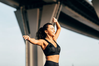 Woman with arms raised exercising while standing outdoors