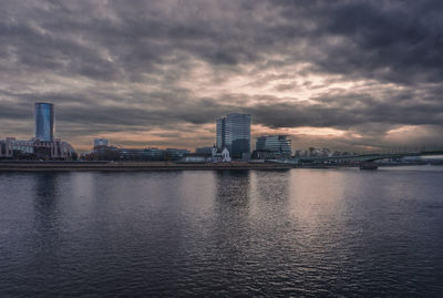 Scenic view of river by buildings against sky during sunset