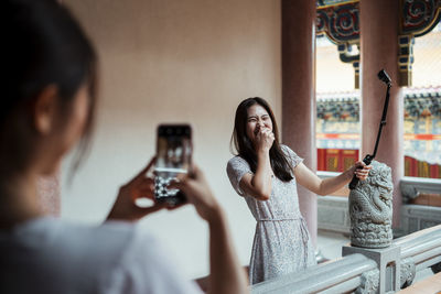 Woman photographing through smart phone while sitting on mirror