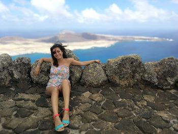 Young woman on rock at beach against sky