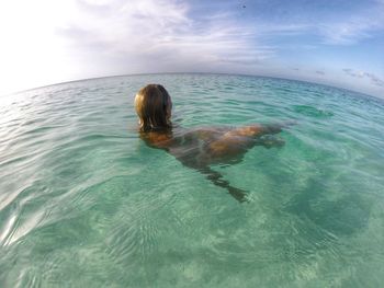 Fish-eye view of woman swimming in sea against sky