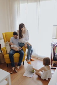 Father with newborn son in yellow armchair. family of four. dad son mom and daughter