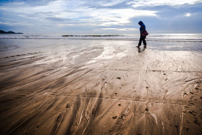 Full length side view of woman walking at sandy beach against sky