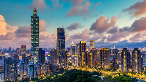 Illuminated buildings in city against cloudy sky