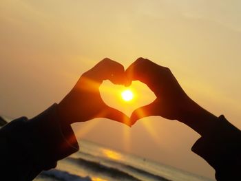 Sun seen through heart shape made by silhouette person during sunset