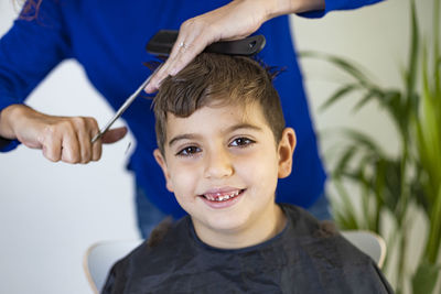 Funny boy getting haircut at home with scissors