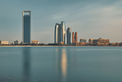 Sea by modern buildings against sky in city