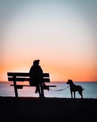 Silhouette woman with dog at beach against sky during sunset