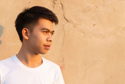 Portrait of young man looking away against wall