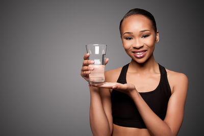 Portrait of young woman drinking water against black background