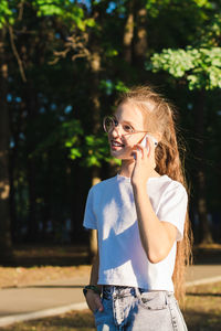 A girl in glasses happily talks on a push-button telephone among the trees vertical view