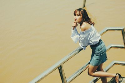 Young woman leaning on railing against sea