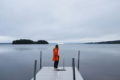 Rear view of woman standing on pier over lake against sky