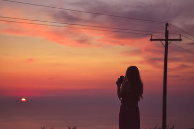 Rear view of woman photographing sunset