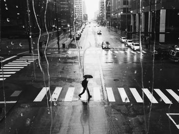 Man crossing road in city during rain seen through wet window