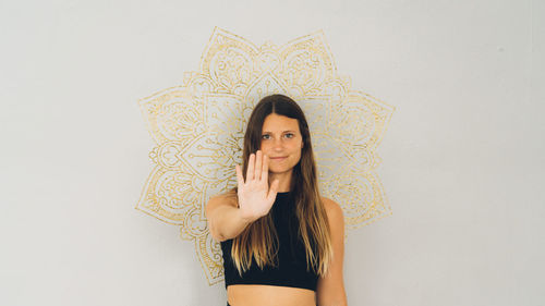 Portrait of young woman standing against wall