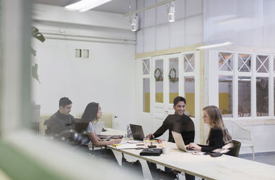 Four people discussing in creative office seen through glass wall