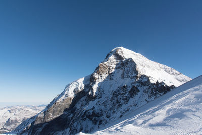 Low angle view of snowcapped mountains against clear blue sky