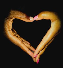 Close-up of woman hand holding heart shape over black background