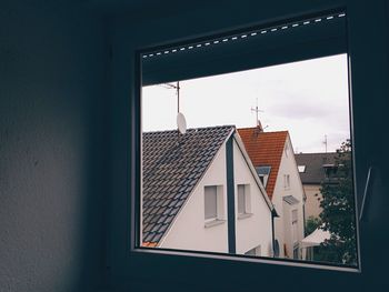 Houses against sky seen from glass window at home