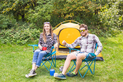 Young couple sitting on grassland against trees