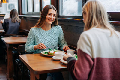 Two women eat in a cozy rustic restaurant and have a friendly conversation.