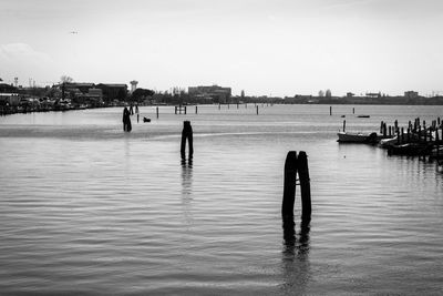 Silhouette people on wooden post in sea against sky