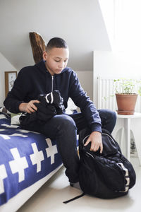 Teenage boy packing clothes into backpack at home