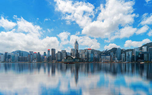 Modern buildings in city by sea against cloudy sky