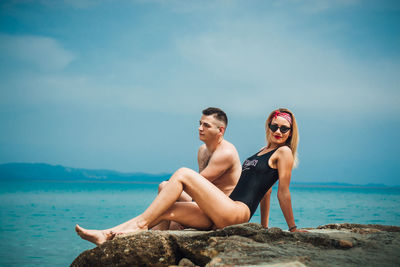 Young couple sitting on sea against sky