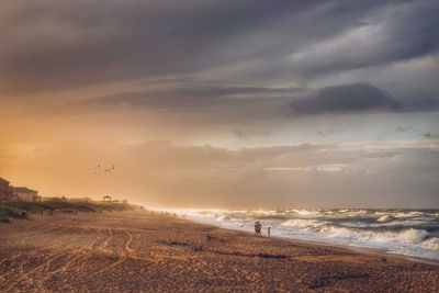 Scenic view of beach against cloudy sky during sunset