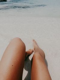 Low section of woman relaxing on sand at beach