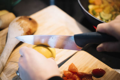 Close-up of hand slicing lemon on cutting board