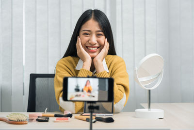 Portrait of a smiling young woman using phone while sitting on table