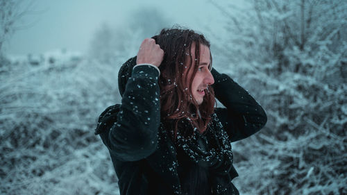 Smiling young man with snow on body standing in forest during winter