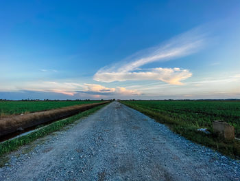 Empty road amidst agricultural field against sky