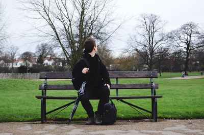 Man with bags sitting on wooden bench against grassy field