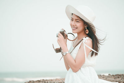 Woman in hat photographing with camera at beach against sky