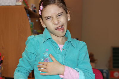 Close-up portrait of girl sticking out tongue while standing at home