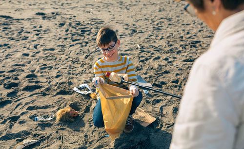 Boy holding sunglasses on sand at beach