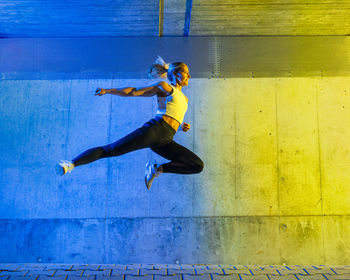 Woman jumping in front of neon colored wall